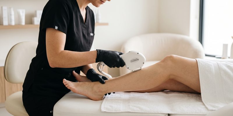 A practitioner in black gloves treating a client's lower leg with the laser handpiece